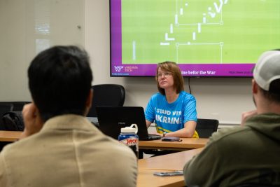 A woman in a blue and yellow shirt that reads "I stand with Ukraine" presents a powerpoint.