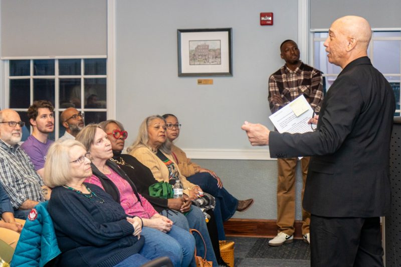 A man speaks to a seated audience in front of him.