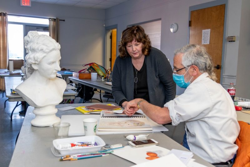 A man and a woman talk over a desk in a classroom.