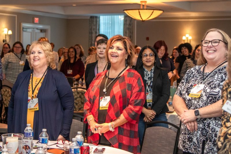 A roomful of participants stand and laugh while looking toward the front of the room.