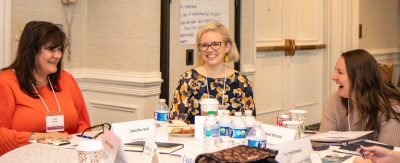 Three women laugh across a round table with each other.