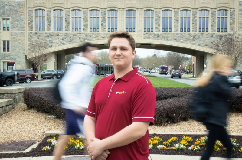 Jackson Ribler stands in front of the Torgerson Bridge and poses for a photo while fellow students walk behind him.
