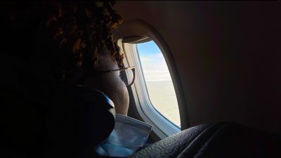 A teen girl looks out the tiny oval window of an airplane.