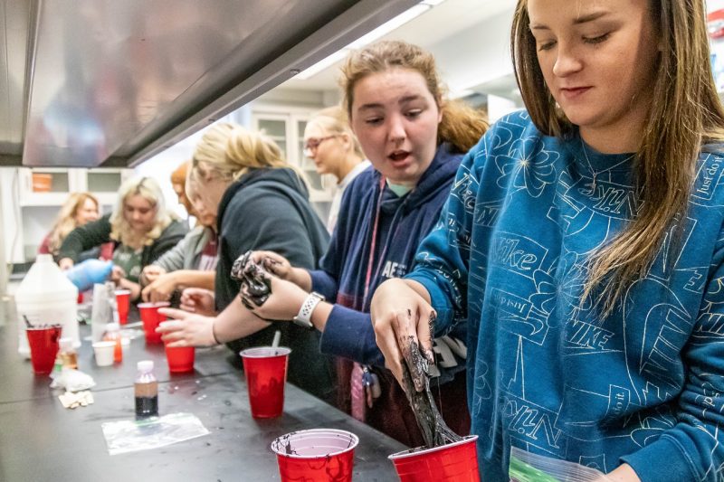 High school girls put their hands into sticky black slime.