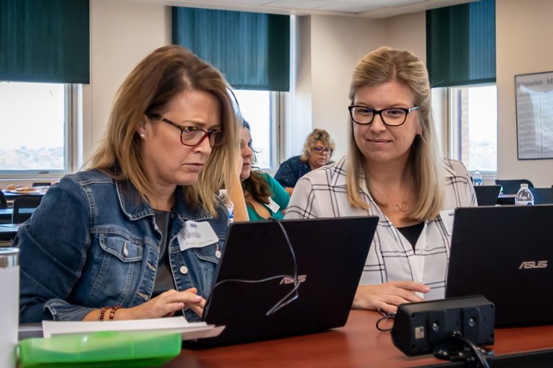 Women Impact Virginia Two women look at a laptop screen sitting on a table in front of them.