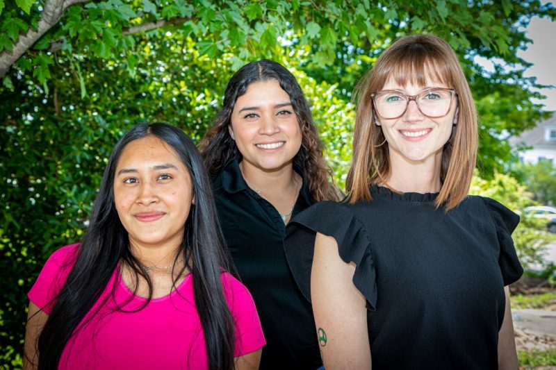 A group of three women pose for a photo under a tree.