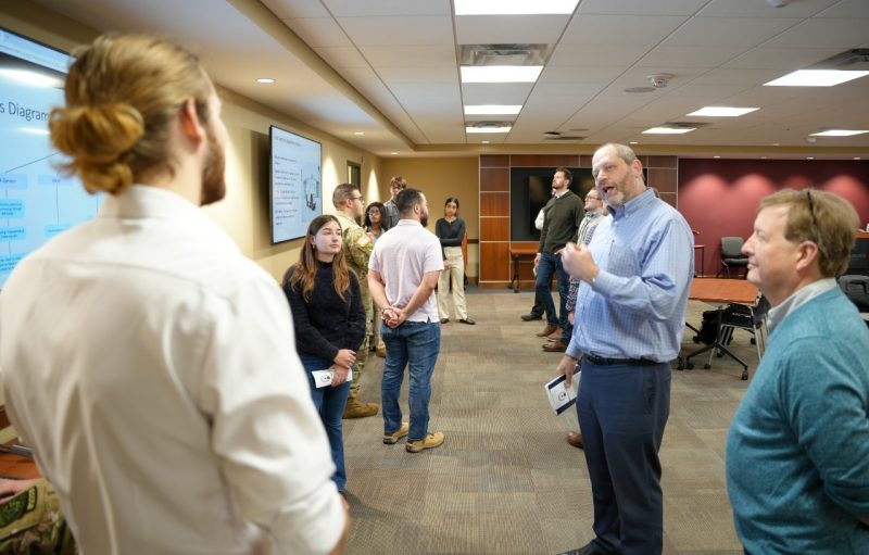 students and reviewers gather around screens where projects are presented