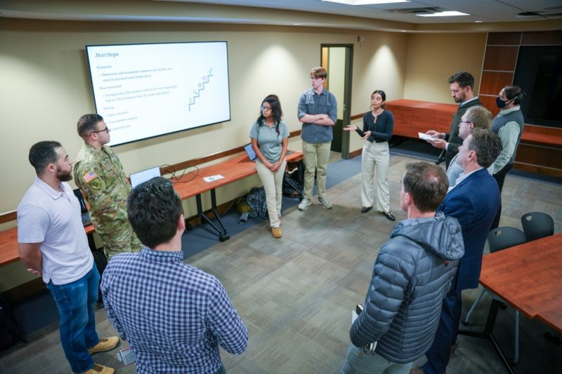 Employees and students gather in a circle to talk about their group projects