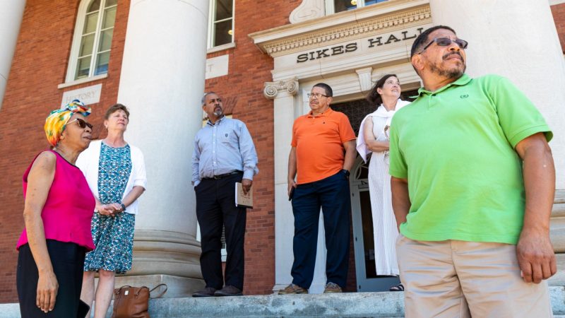 outreach-clemson A group of people stand on the steps of a big brick building under a sign that reads "Sikes Hall."