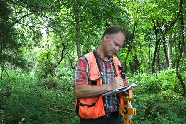 CNRE Downing Fieldwork A person writes notes on a notebook while standing in a forest.