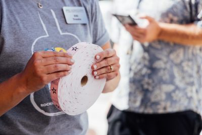 67_20240914_UtProsim_ElliTravis_CF_8477.jpg Hands hold a roll of pink tickets.