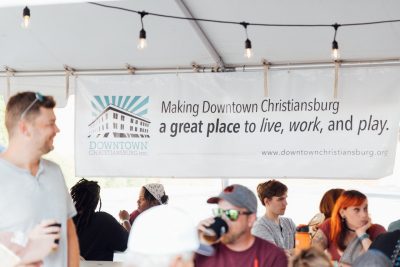 73_20240914_UtProsim_ElliTravis_CF_8639.jpg People sit at long tables in front of a banner that says "Making Downtown Christiansburg a great place to live, work, and play."