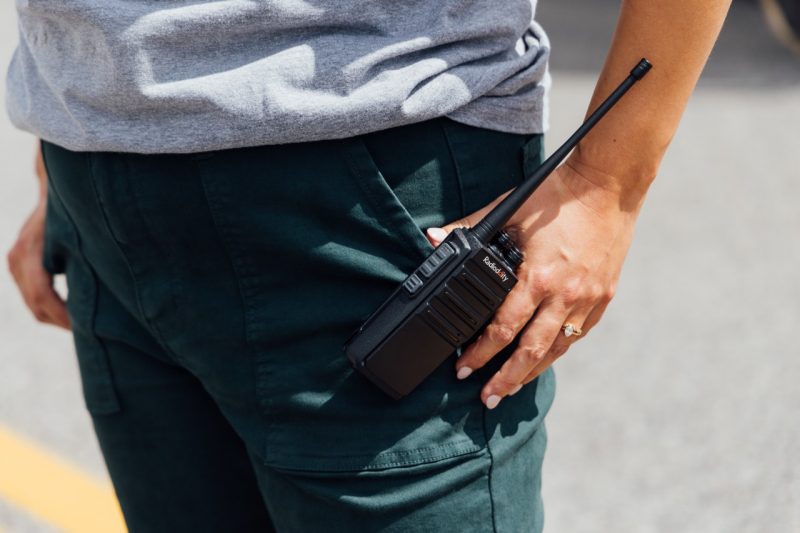 20240822_UtProsim_TJones_CF_4357.jpg A close up of a walkie-talkie on the outside of a pants pocket, a hand rests on it.