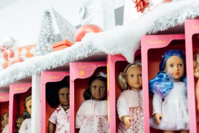 A row of American Girl-style dolls in pink boxes on a shelf