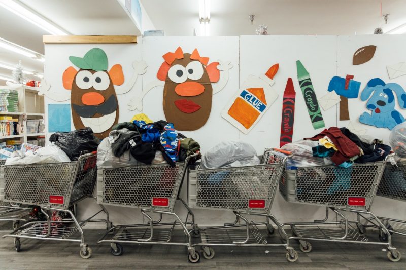 A row of four shopping carts piled high with clothing sit before a wall with paper decorations of Mr. and Mrs. Potato Head, crayons, glue, and Blue from Blue's Clues.