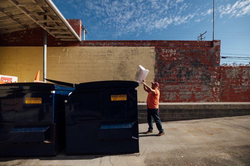 John Tarter throws trash in a dumpster next to the Christmas Store.
