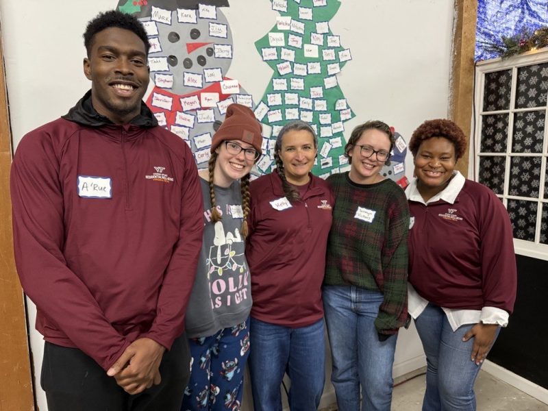 Four students and a staff smile in front of a winter-decorated wall.