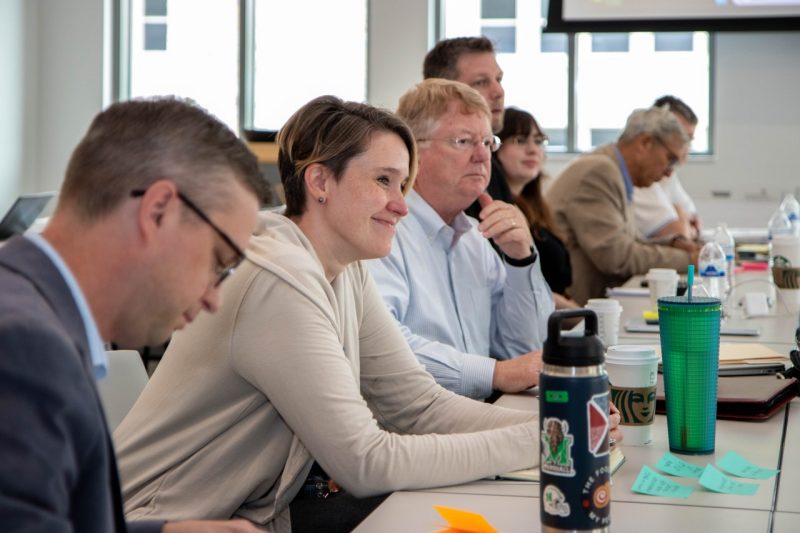 People sit at a table with Sarah Lyon Hill leaning forward and smiling.