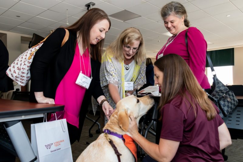 Four women surround a yellow lab, who is sitting on the floor.