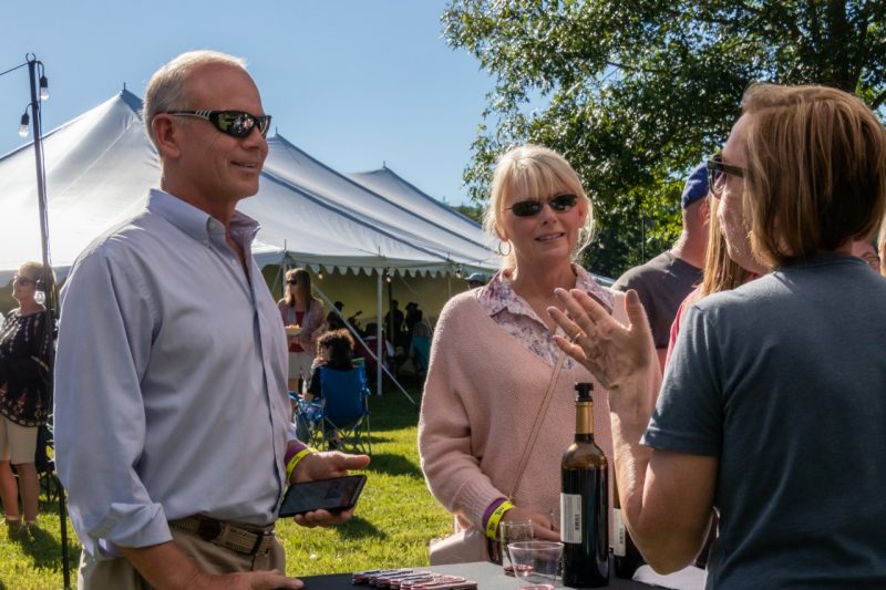 A man and woman talk to a woman about wine as the bottle sits between them.