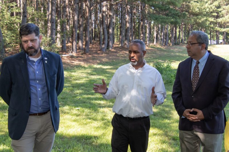 Three men standing talking in a shaded wooded area