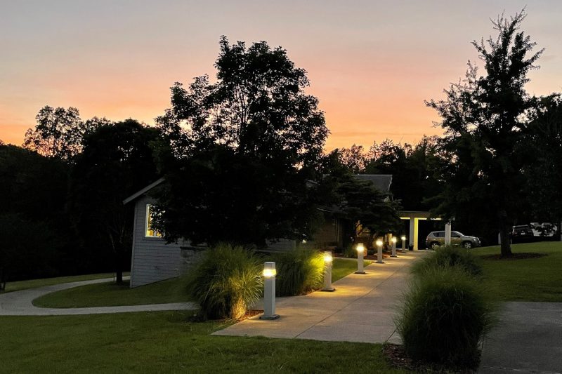 Lights lead the path to the front door of the community building as the sun sets in the background.