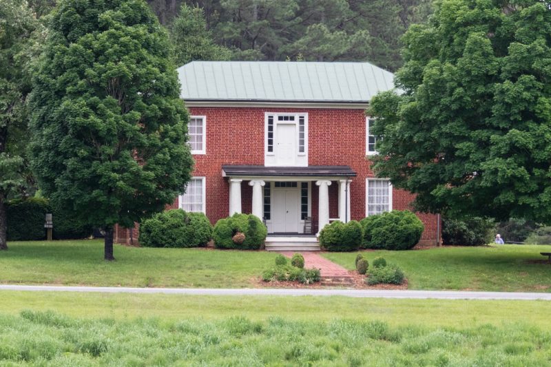 Old brick house with white columns and surrounded by green leafy trees.