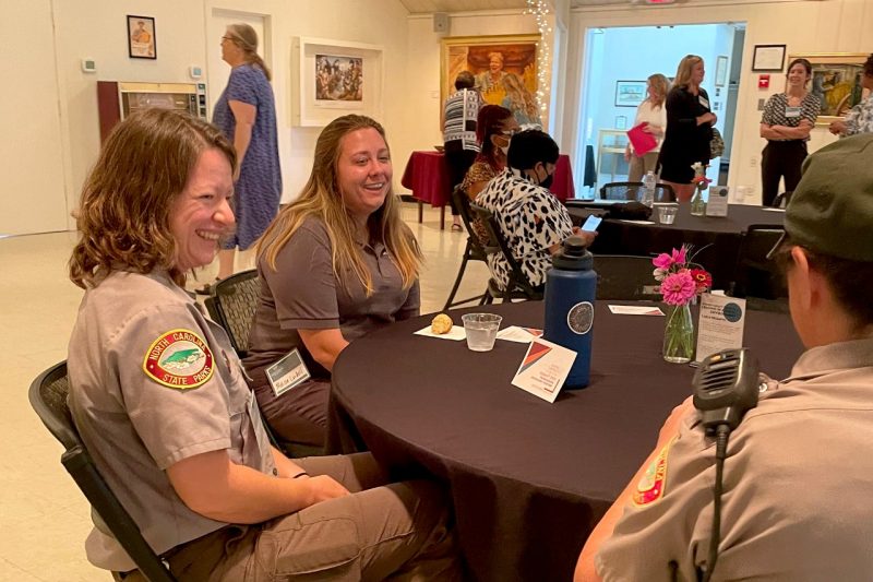 Women in uniform talk to one another at a table.