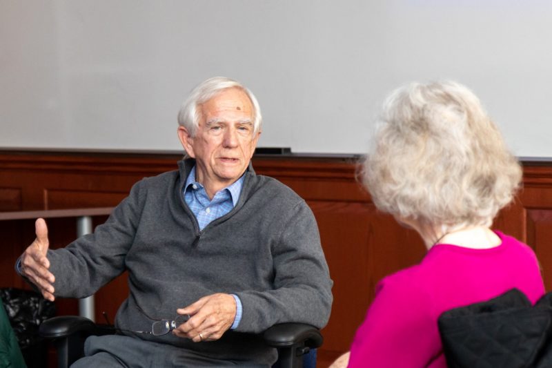 A man sits in a desk chair talking to a woman.