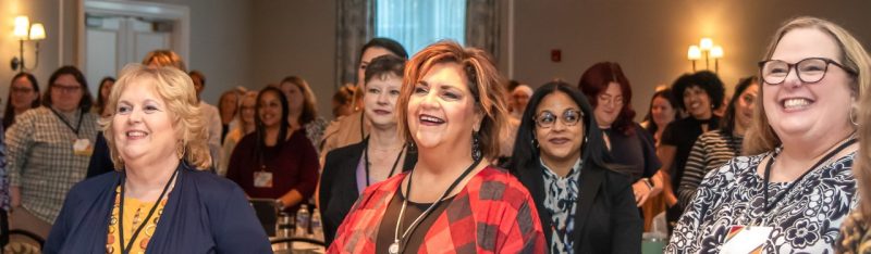 Three women, with a roomful of others behind them, stand and applaud during the summit