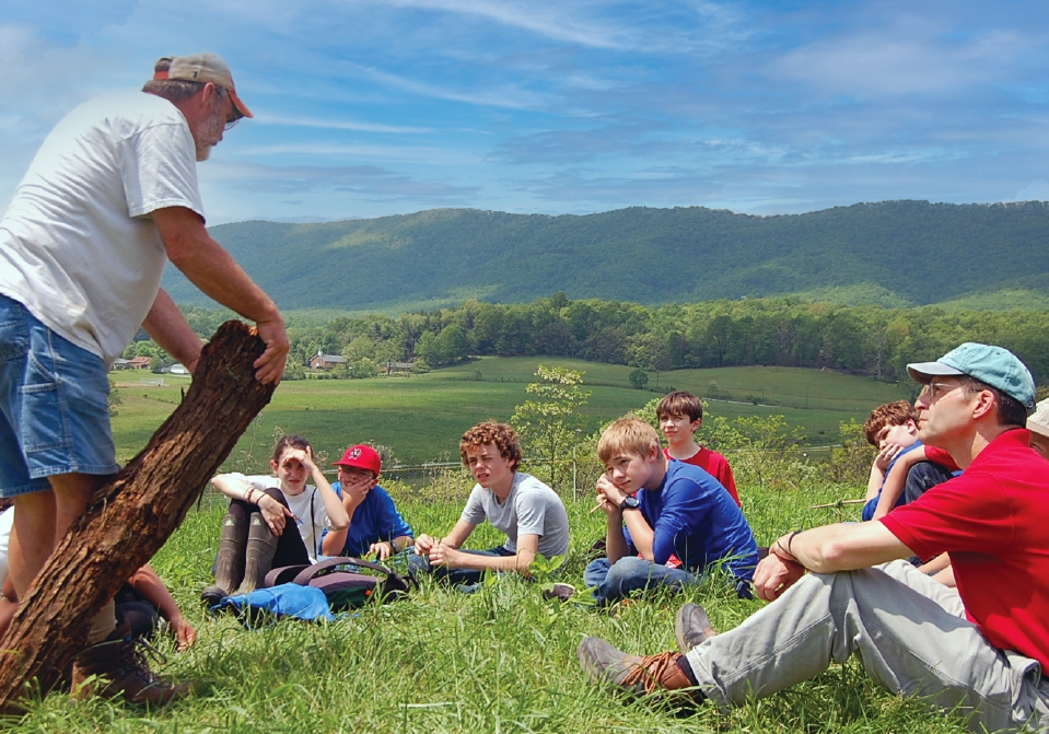 A man standing in a field surrounded by students sitting in the grass