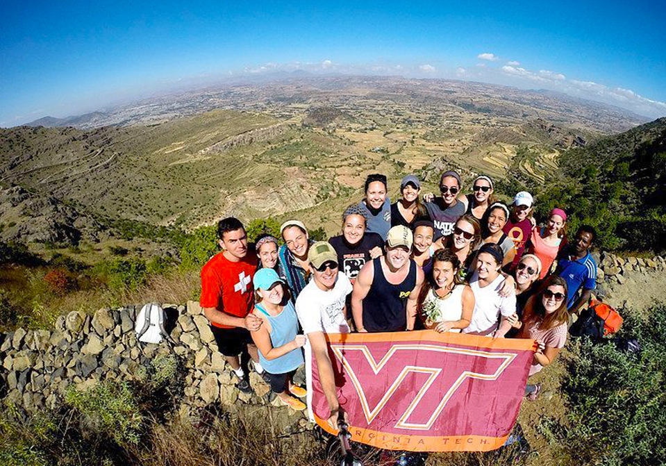 Students standing on a mountain and holding a VT flag