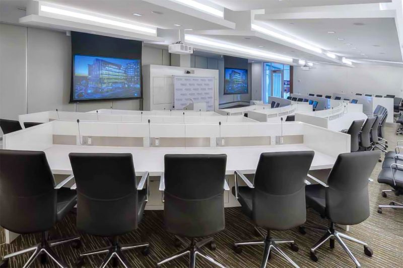 A large meeting room with twin screens at the front displaying the outside of the building.