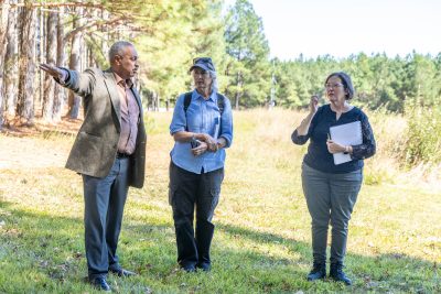 Three people stand in a field talking.