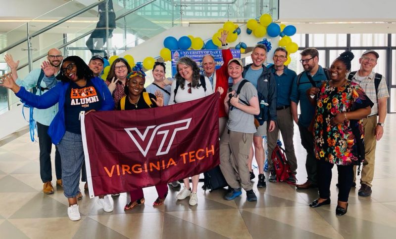 A group of thirteen people holding a Virginia Tech flag in an airport
