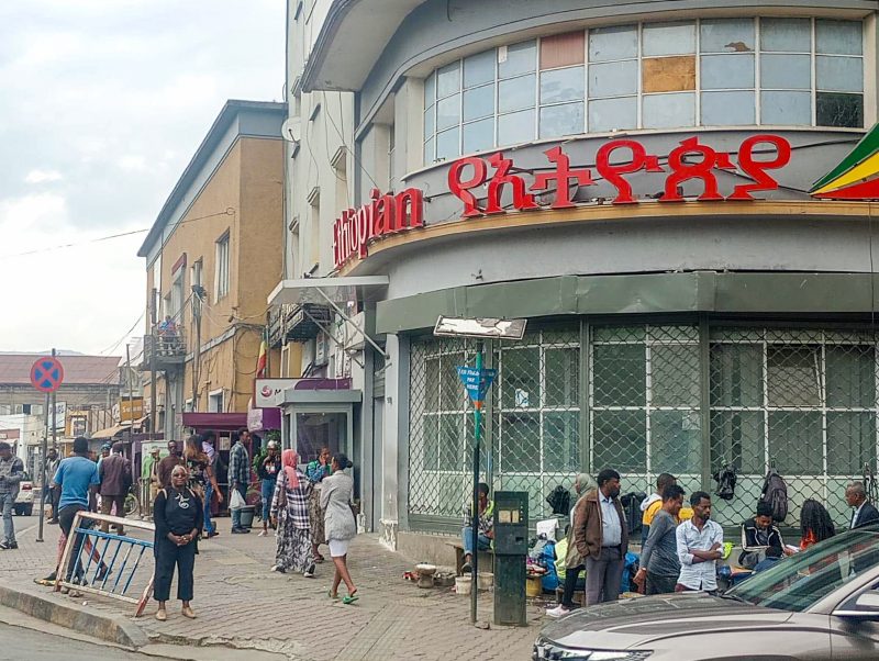 A woman standing in front of a shop and next to a busy road